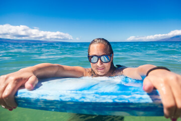 Beautiful Surfer girl floating in the ocean on her surfboard on a gorgeous sunny day. Cool reflection off her sunglasses. Horizontal photo with copy space