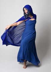 Full length portrait of beautiful female model wearing elegant fantasy blue ball gown and flowing cape with hood. Standing pose, with gestural arms reaching out . Isolated on white studio background. © faestock