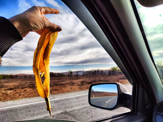 A woman's hand holds a banana skin near an open car window and throws it away. Garbage,...