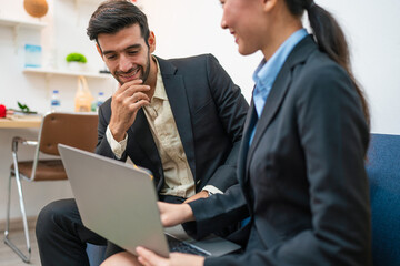 Two happy business woman and man using laptop working on computer at workplace. Cheerful young professional multiethnic colleagues team discussing online digital technology corporate project in office