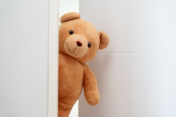 Cute brown Teddy bear toy sneak behind the door and surprise to congratulate the special day holiday festivals. game child, day care, welcome, kid day, shy childhood, party funny, stuffed doll - obrazy, fototapety, plakaty