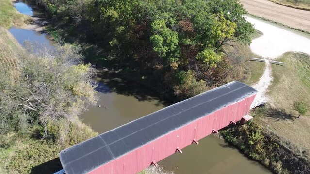 Hogback covered bridge in Madison County Iowa. Aerial flyover shot that angles over the bridge and stream below it. Bright sunny afternoon.