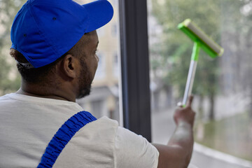 Man in cap uses special tools for washing windows and scraper for cleaning glass. An employee of...