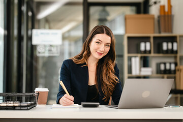 Attractive professional caucasian businesswoman working on her laptop, likely in an office setting, Balance Sheet, Accounting of Owners Equity, Cash Receipts Journal, Liabilities, Idle Capacity - obrazy, fototapety, plakaty