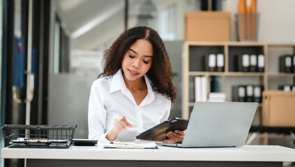 African American businesswoman, focused on her work on a laptop, possibly managing industrial...