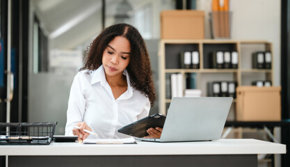 African American businesswoman, focused on her work on a laptop, possibly managing industrial production tasks.