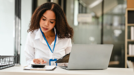 African American businesswoman, focused on her work on a laptop, possibly managing industrial production tasks.