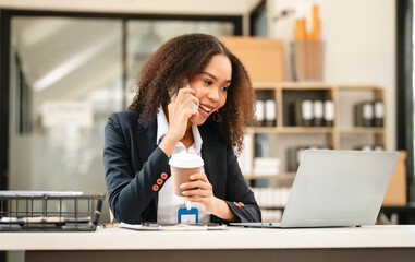African American businesswoman, focused on her work on a laptop, possibly managing industrial...