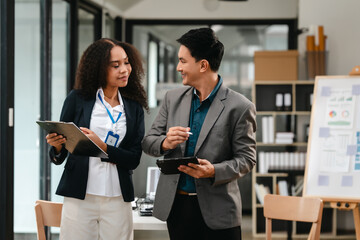 Confident Asian businessman and African American businesswoman reviewing and discussing UX/UI design elements together at desk. in formal suit