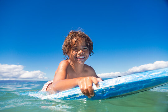 Close up low-angle view of a Smiling diverse young boy boarding in the beautiful blue ocean. Enjoying a fun day playing at the beach while on vacation