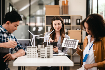 Diverse team with Asian man, African American woman, Caucasian woman discussing a clean energy city planning project with building models and solar panels.
