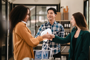 Obraz premium Diverse team with Asian man, African American woman, Caucasian woman discussing a clean energy city planning project with building models and solar panels. Shaking hands