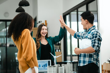 Diverse team with Asian man, African American woman, Caucasian woman discussing a clean energy city planning project with building models and solar panels.