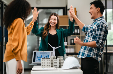 Diverse team with Asian man, African American woman, Caucasian woman discussing a clean energy city planning project with building models and solar panels.