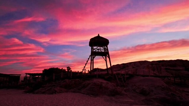 Silhouette of wooden lifeguard stand at tropical beach with pink red clouds at sunset, Cabo Pulmo
