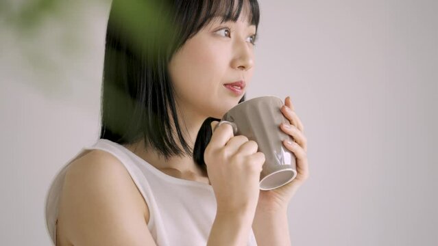 マグカップで飲み物を飲む白い服の若い女性