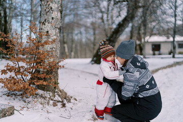 Fototapeta na wymiar Little smiling girl stands near squatting mother in snowy park