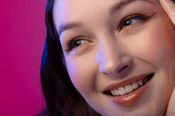 Caucasian woman wearing eyeliner and lip gloss on pink background