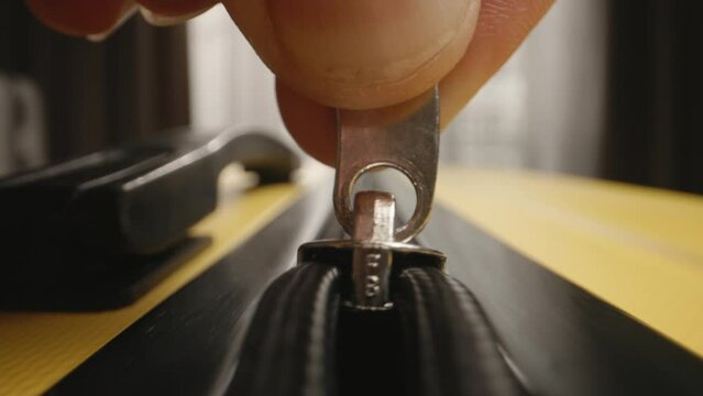 Zipper on suitcase. Unzipping yellow travel luggage. Unrecognizable male fingers pull zipper tab. Start of memorable trip, weekend getaway, escape routine, indulge in relaxation and adventure. 