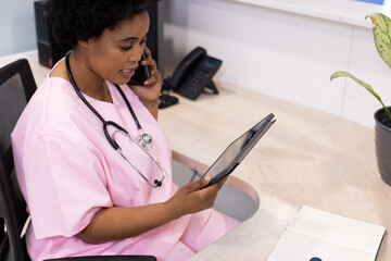 African american female doctor talking on smartphone and using tablet in hospital reception