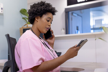 African american female doctor talking on smartphone and using tablet in hospital reception