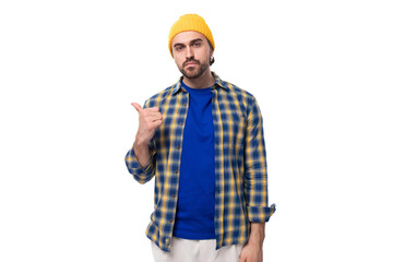 young european brunette man with a beard and mustache dressed in a yellow cap and a blue shirt points his hand to the side