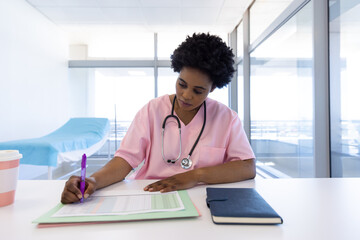 African american female doctor writing in sunny hospital office