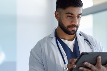 Biracial male doctor using tablet in sunny hospital room