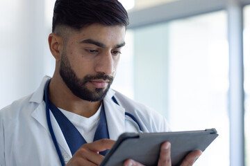 Biracial male doctor using tablet in sunny hospital room