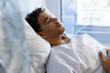 Biracial male patient sleeping in bed in sunny hospital room