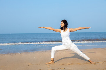 Beautiful young indian woman wearing white sports wear practice yoga at the beach. Young girl stretching muscles, Healthy Lifestyle Concept.