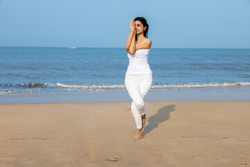 Beautiful young indian woman in white sports wear doing yoga at the beach. Healthy Lifestyle Concept. Copy space