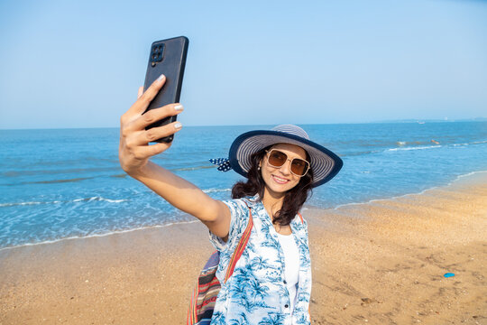 young Indian girl in summer casual clothes taking a selfie picture with smart phone at beach. Travel, vacation concept.