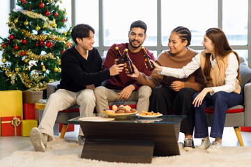 Millennial Asian Indian multinational cheerful male female friends celebrating Merry Christmas Eve Happy New Year  cheers toasting beers in living room full festival decoration with Xmas tree