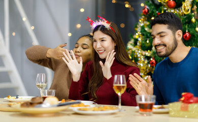 Group of Asian Indian happy cheerful male female friends wears reindeer antlers headband happy meeting with champagne beverage glasses together on dinner table celebrating Christmas eve in dining room