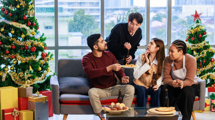 Asian Indian male female friends  sitting on sofa smiling meeting party talking together in living room fully decorated party with Xmas tree