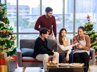 Asian Indian male female friends  sitting on sofa smiling meeting party talking together in living room fully decorated party with Xmas tree
