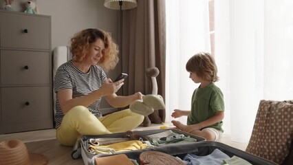 In anticipation of trip, mom and child meticulously organize their belongings. Utilizing smartphone application, they ensure all items are packed accurately and efficiently for their adventure 