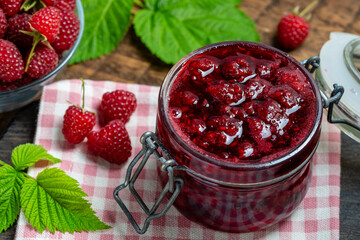 Red raspberry jam and fresh raspberry on a wooden table. Rustic style, closeup