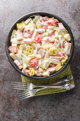 Grinder salad is made with lettuce, salami, provolone, and fresh veggies, all coated in a creamy, savory dressing closeup on the plate on the table. Vertical top view from above
