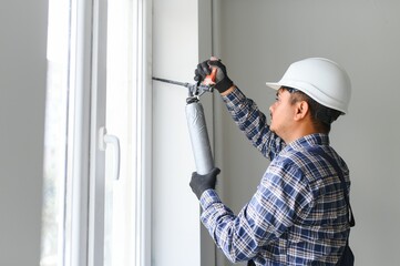Indian worker using a silicone tube for repairing of window indoor - obrazy, fototapety, plakaty