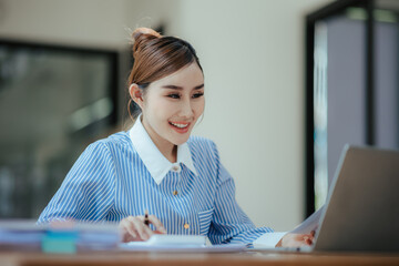 Portrait of beautiful Asian businesswoman sitting in office, data, documents, laptop computer on table. Female analyst analyzing the market, planning financial business. business success