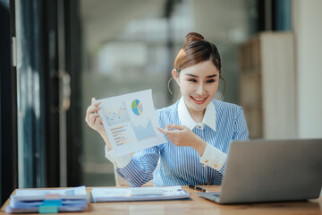Fototapeta premium Portrait of beautiful Asian businesswoman sitting in office, data, documents, laptop computer on table. Female analyst analyzing the market, planning financial business. business success