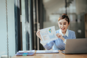 Portrait of beautiful Asian businesswoman sitting in office, data, documents, laptop computer on...