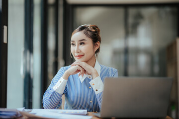 Portrait of beautiful Asian businesswoman sitting in office, data, documents, laptop computer on table. Female analyst analyzing the market, planning financial business. business success