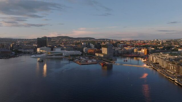 Amazing picturesque aerial view of bay in city at golden hour. Buildings on waterfront lit by low sun. Munch museum and Oslo Opera House. Oslo, Norway
