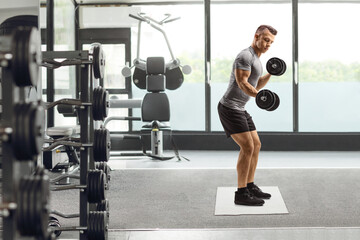 Fototapeta na wymiar Young fit man lifting dumbbells at a gym