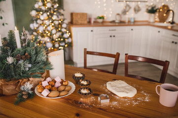 Homemade Christmas cookies on a decorated wooden table in the kitchen. Raw dough, muffin tins, chocolate chip cookies are prepared before Christmas by the whole family