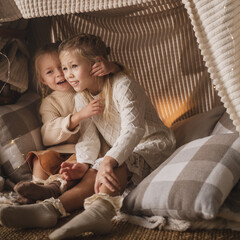 two little girls, blonde sisters in light elegant sweaters and dresses, play at home near the New...
