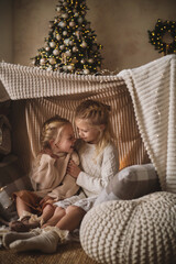 two little girls, blonde sisters in light elegant sweaters and dresses, play at home near the New...